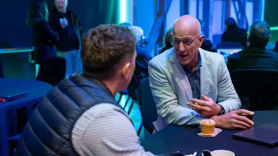 Two attendees in conversation over coffee at a Roadshow table session